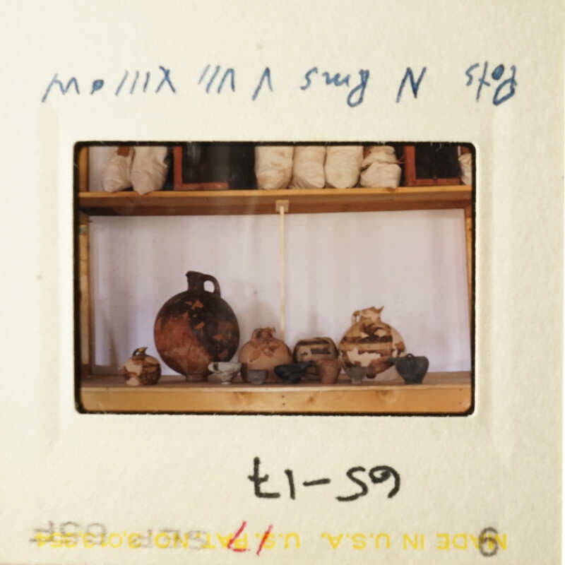 The photo shows an antique camera with a vintage design, capturing a scene inside a room filled with pottery and ceramics on shelves, with a focus on vases of different shapes and sizes.