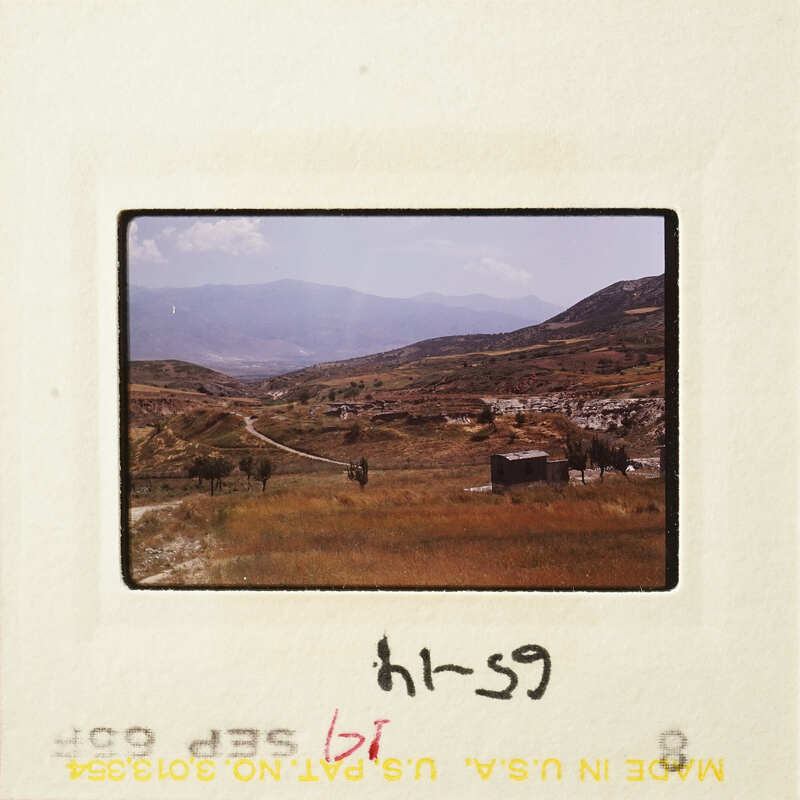 A photograph of a mountainous landscape with a dirt road and sparse vegetation.