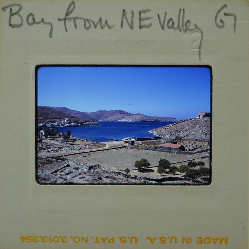 A vintage photograph of a coastal village with mountains and blue water.