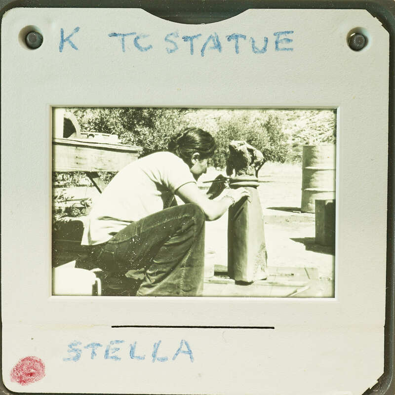 Person crouching next to a large terracotta statue. 