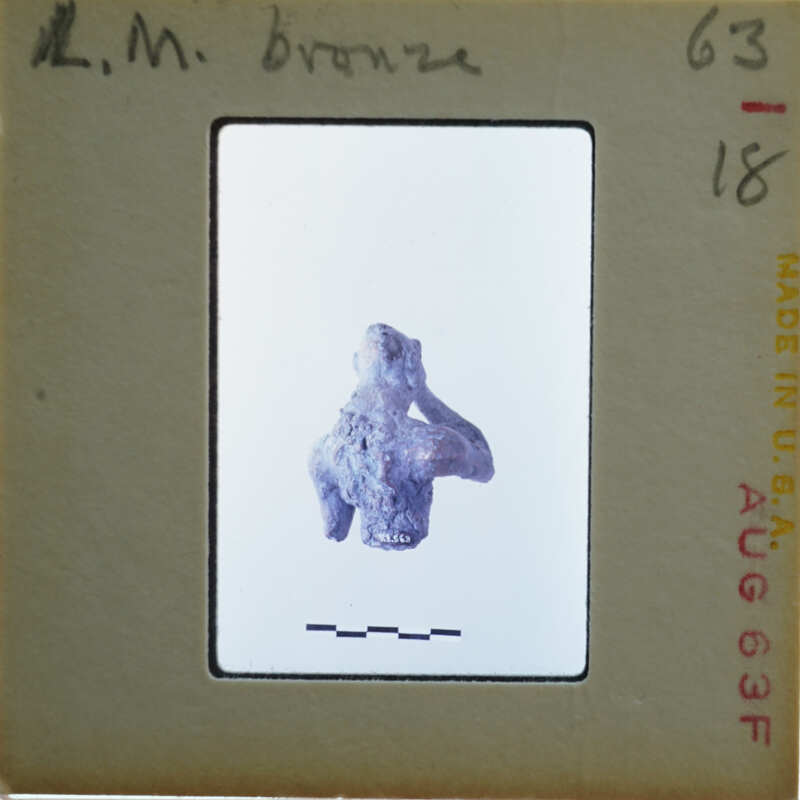 Small, ancient sculpture with a damaged head displayed on a card.