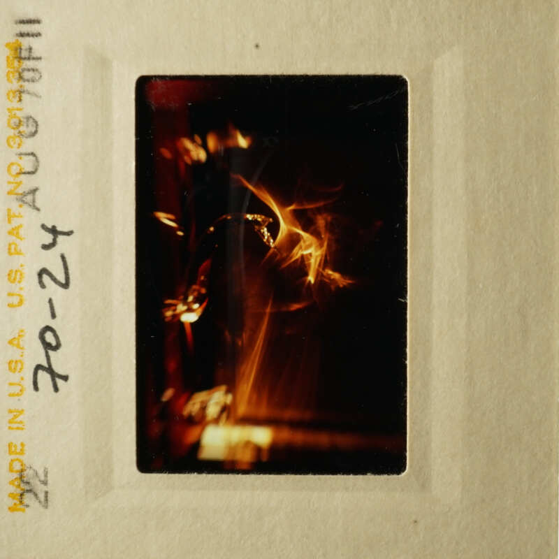 This is an image of a photograph with a yellowish hue, featuring what appears to be a close-up of a flame or light source, possibly from a candle or fireplace, with a darker background.