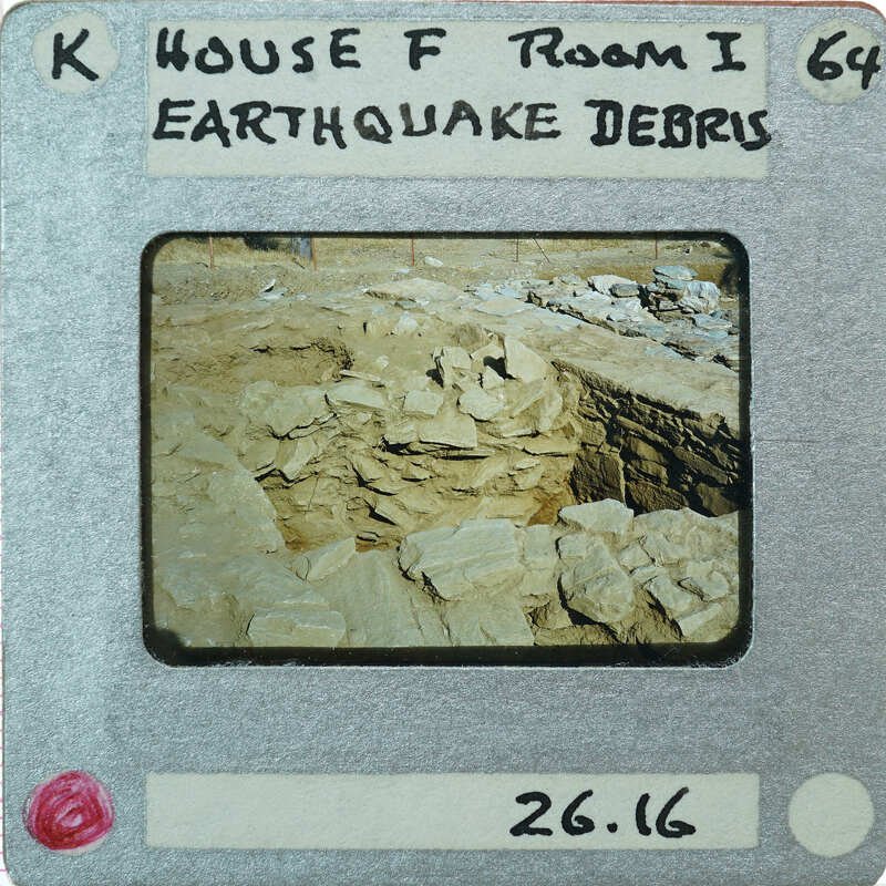The image is a photograph of an earthquake-damaged area with debris and rubble, captured on a faux filmstrip label.