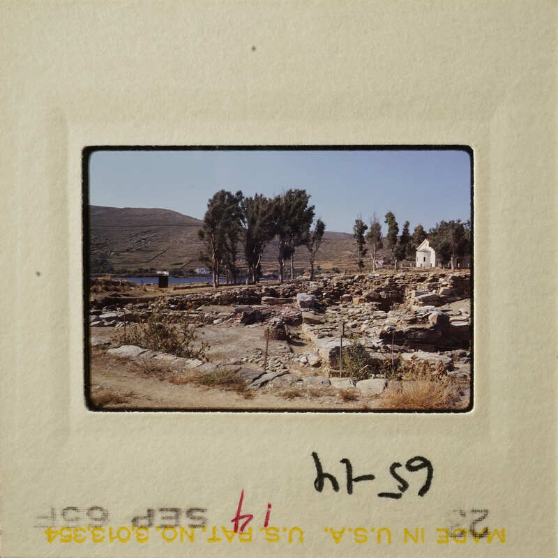 Ancient ruins with stone structures and trees, set against a mountainous landscape.