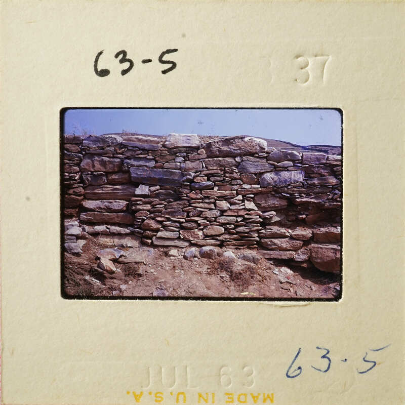 Old stone wall with weathered stones and dirt ground.