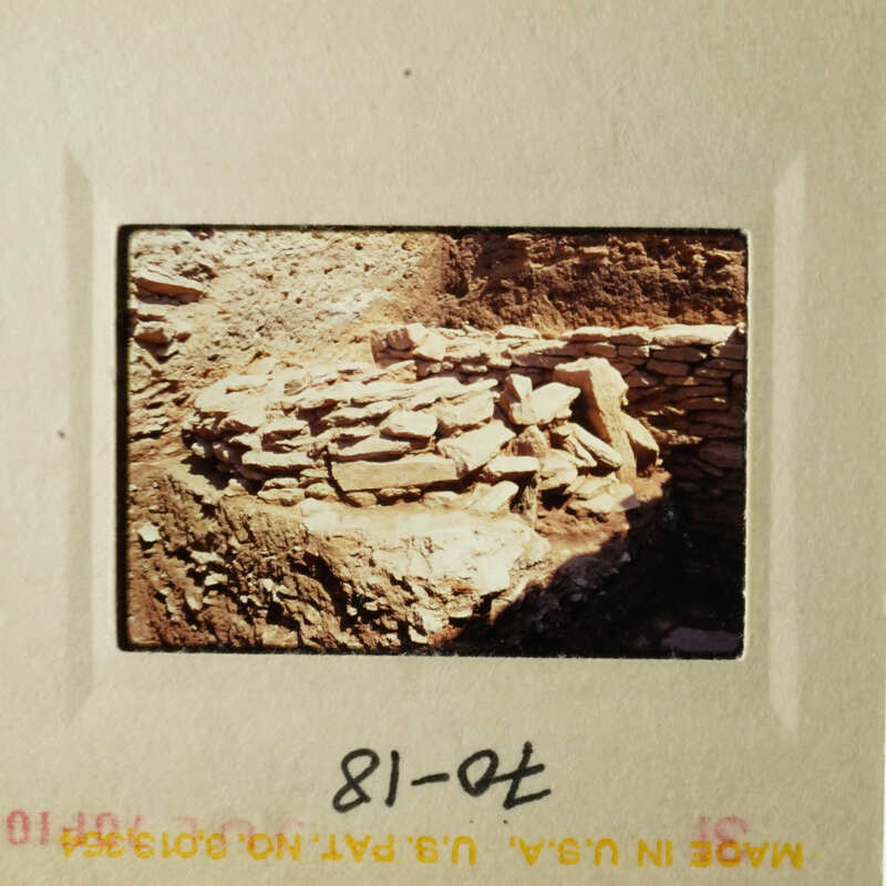 This is an old photograph depicting a rock wall and stone ruins, likely taken from a distance.