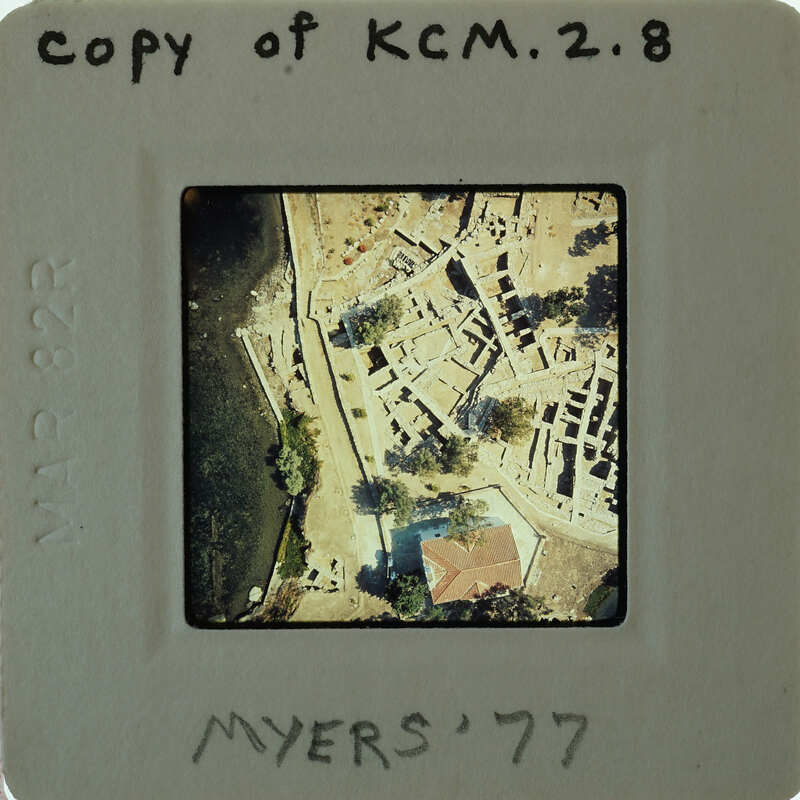 The image is a photograph of an archaeological site with ruins, surrounded by water.