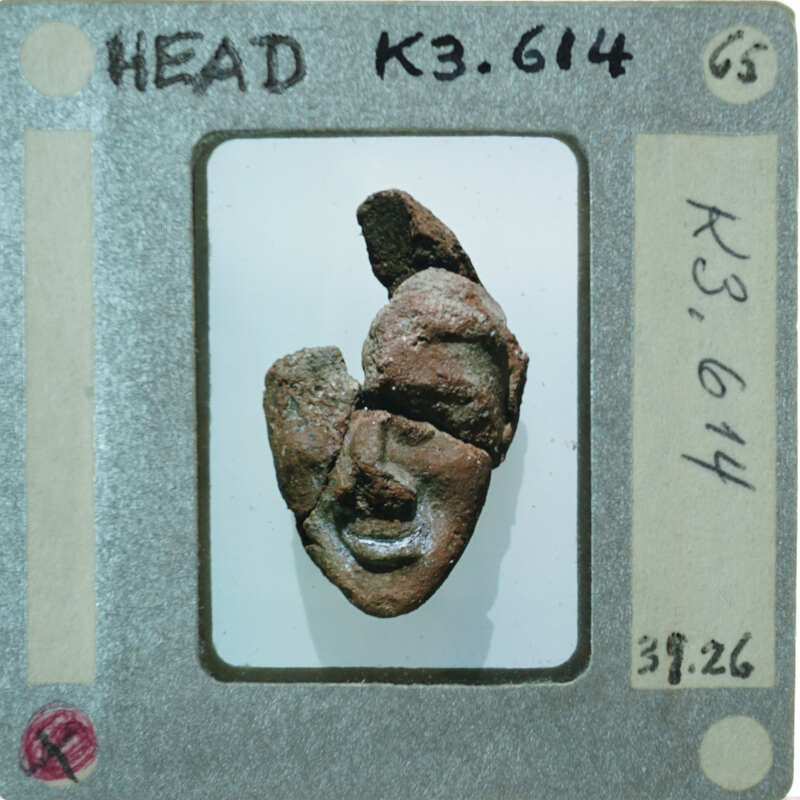 A small, broken clay figurine displayed on a piece of paper with handwritten notes.