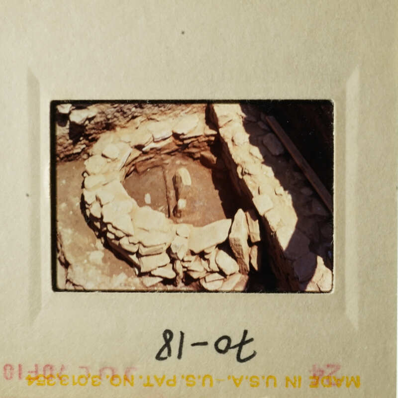 Image shows an ancient stone structure, possibly a well or pit, with stones around it, set against a natural backdrop.