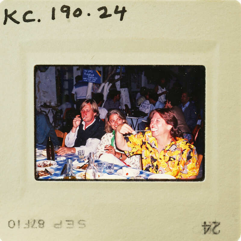 A vintage photo of three people sitting at a restaurant table, smiling and enjoying their time together. Catalog number KC.190.24
