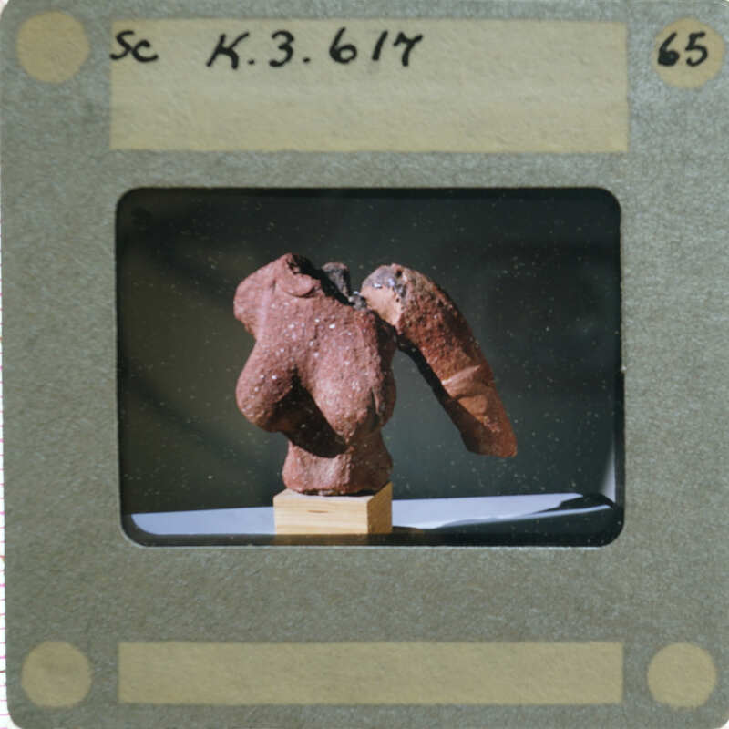 A photograph of a clay figurine torso, displayed on a stand.