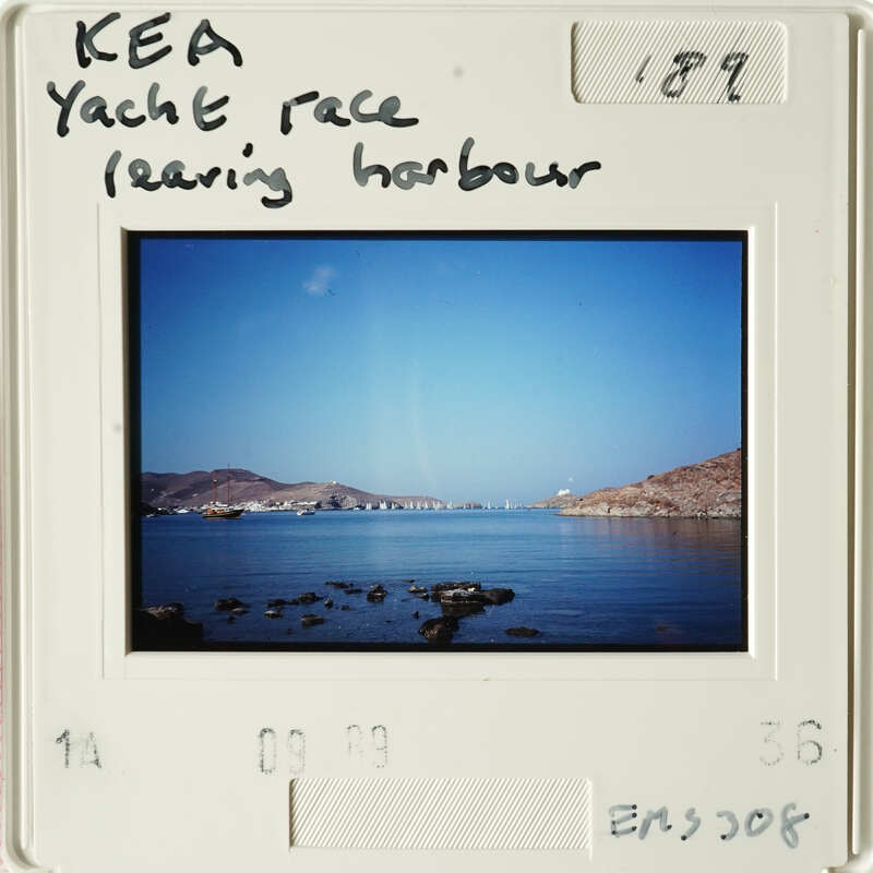 Landscape photograph showing calm waters with distant mountains and boats, viewed from a coastal perspective.