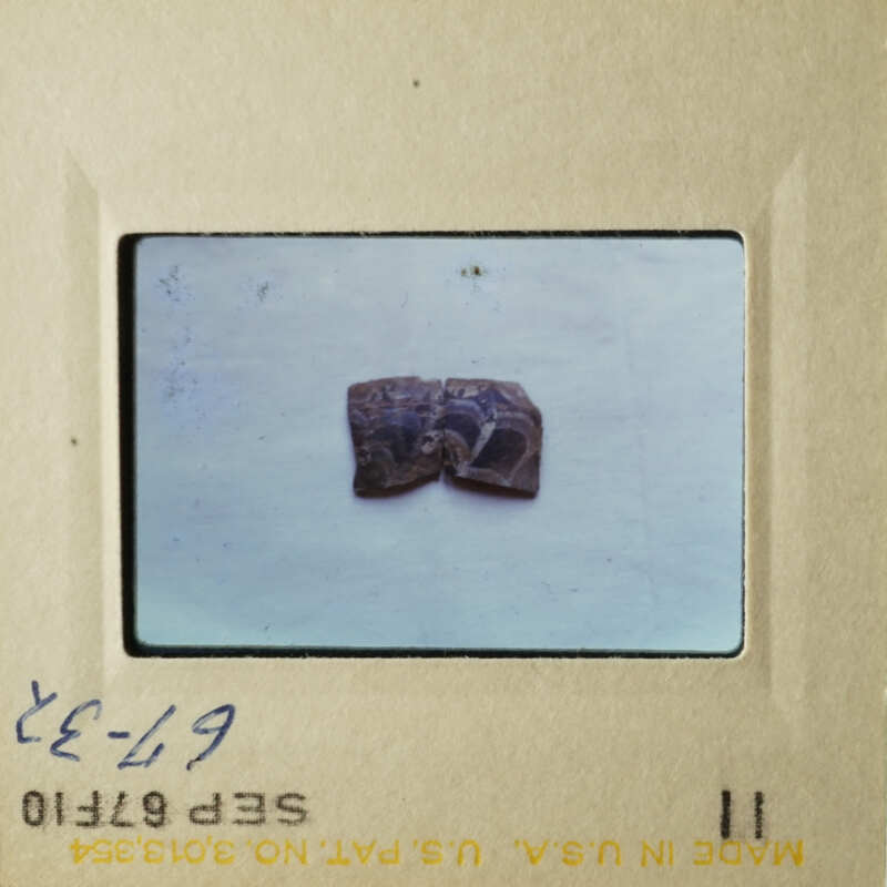 The image shows a small, dark object on a white surface, possibly a piece of jewelry or an artifact, with two photographs side by side.