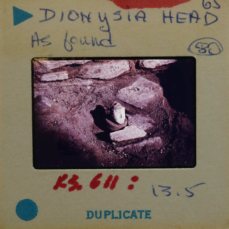 Terracotta figurine head on surface with walls.