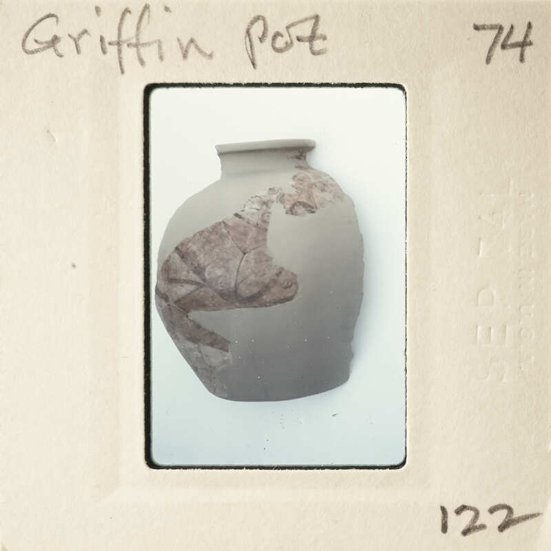 A photograph of a clay pot with a leaf-like design on it.