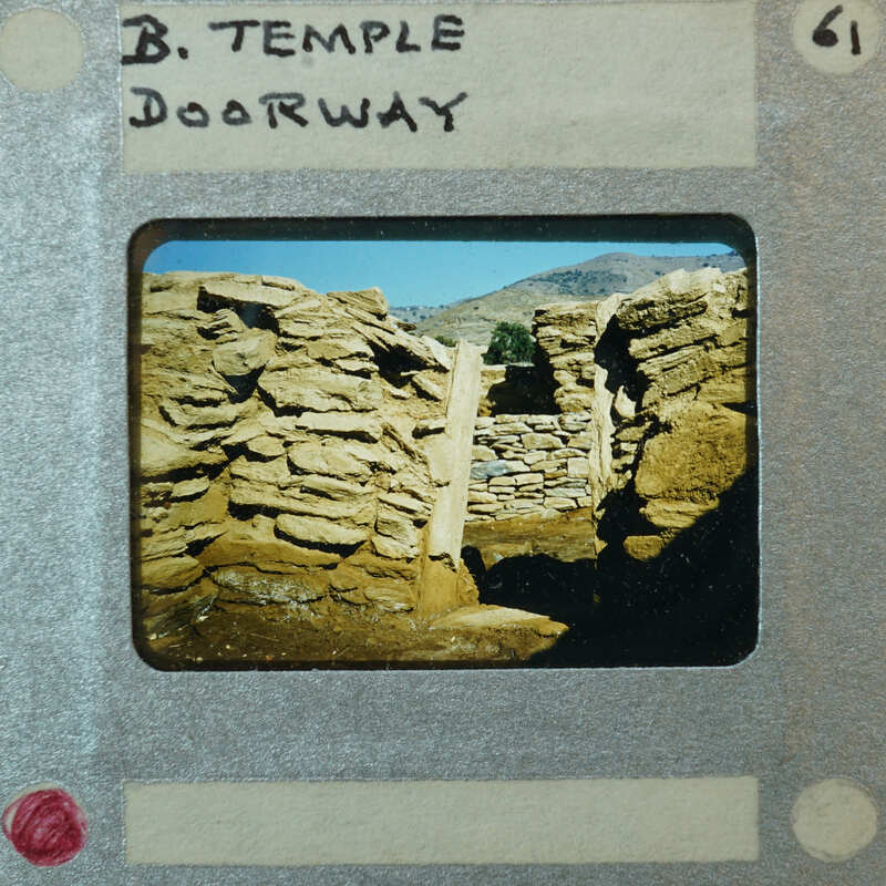 Detail of stone walls forming a doorway with mountains and sky in the background.