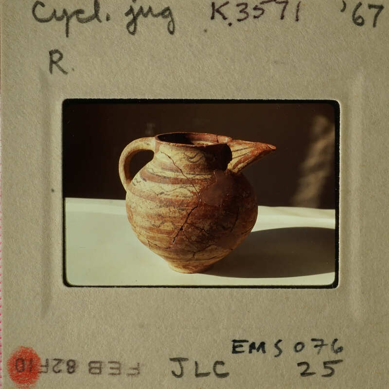 Ancient clay pot with two handles and a spout, sitting on a white surface.