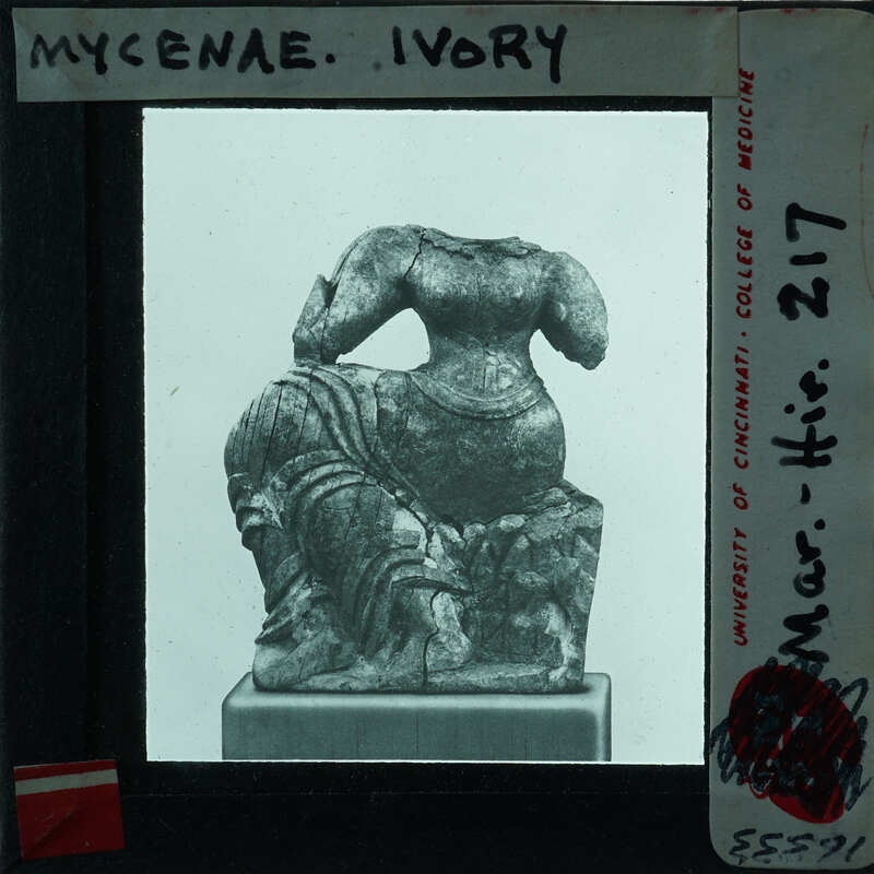 Ancient sculpture of a seated figure, possibly from the Mycenaean period, displayed on a pedestal with an information card.