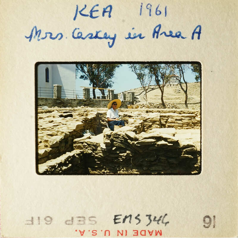 Woman sitting on ancient ruins with Mediterranean landscape in background.