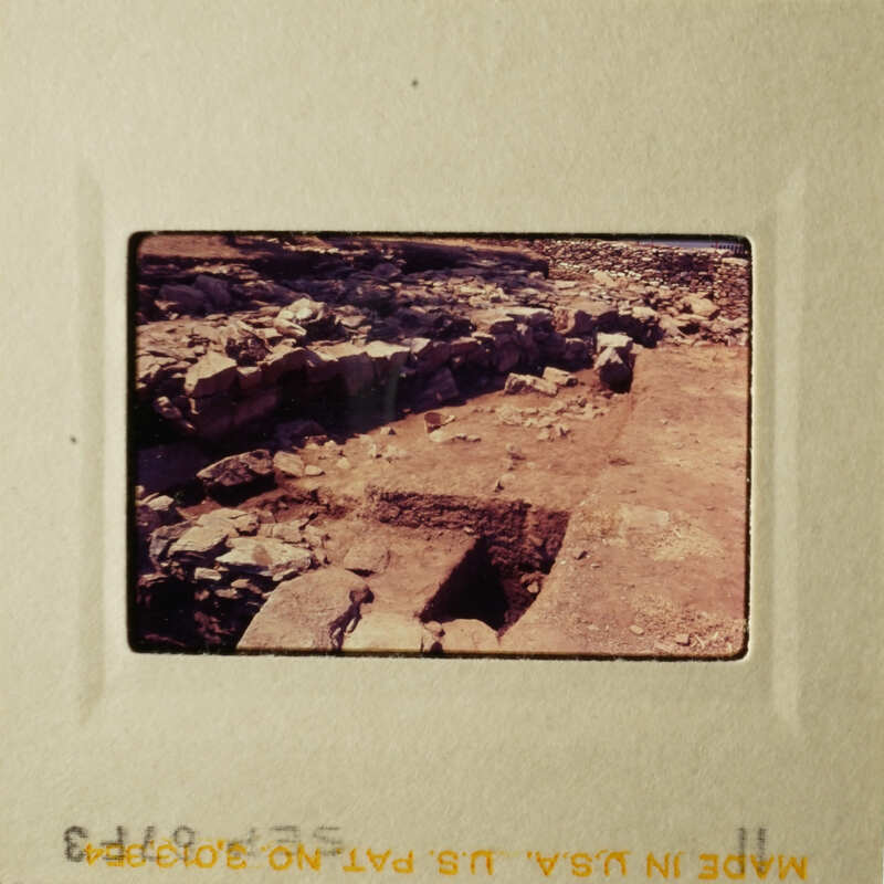 This is an image of an ancient stone structure, possibly ruins, with a dirt ground and a clear sky above.