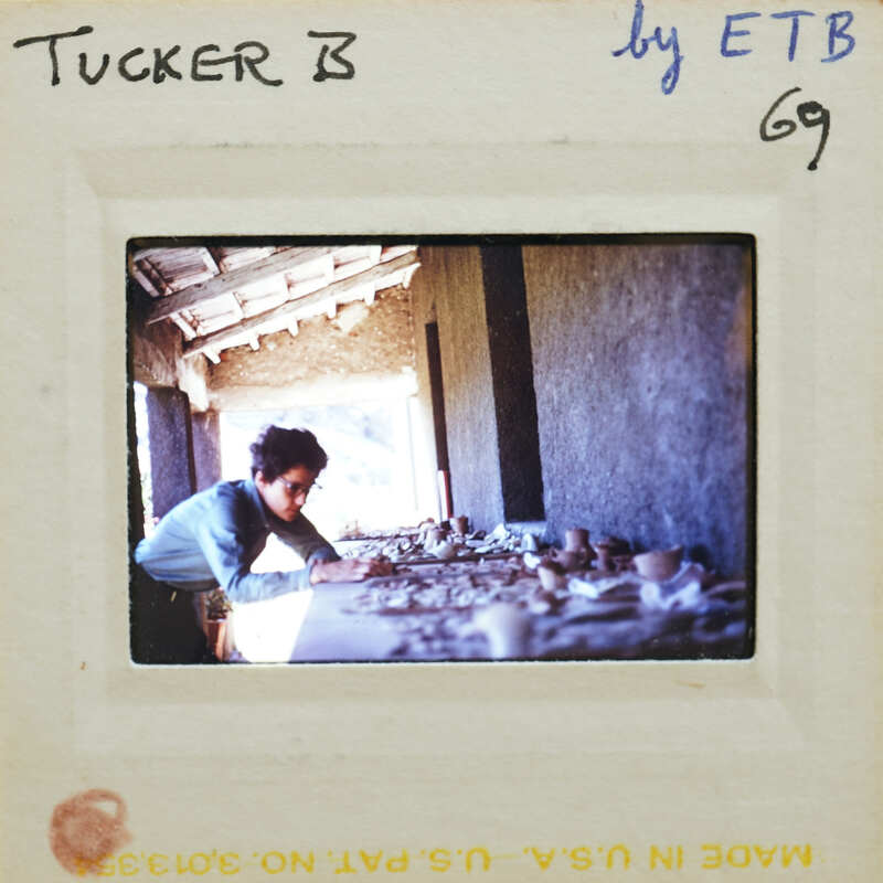 A person working on a pottery wheel with clay, surrounded by finished pieces.