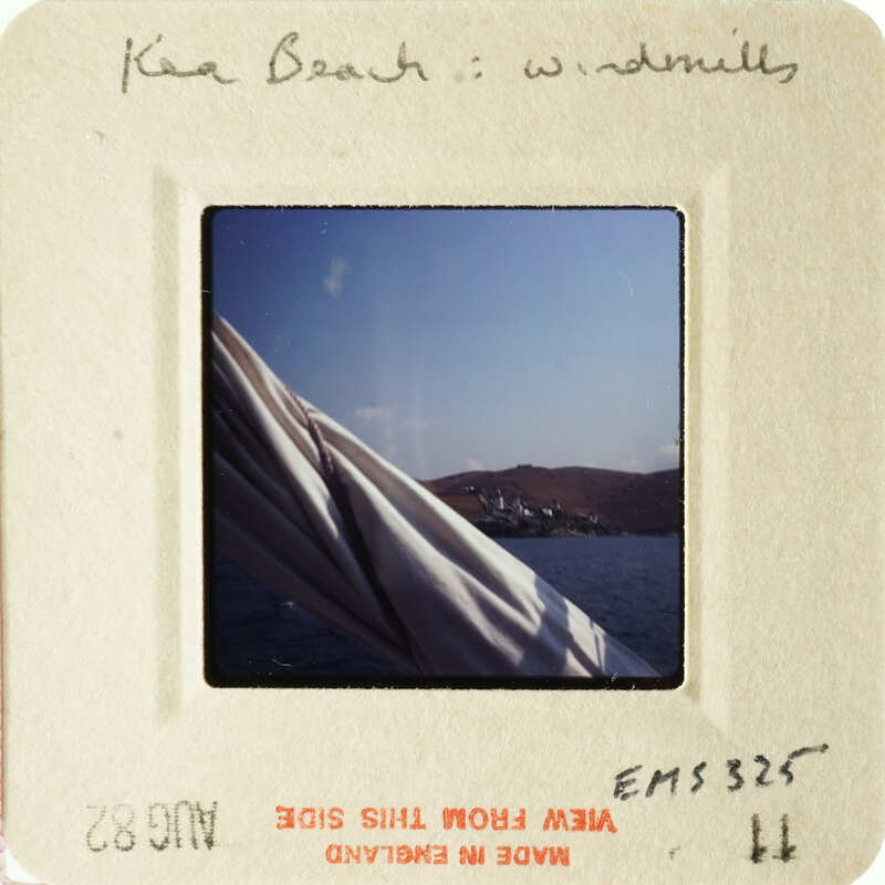 A photograph of an ocean scene with a windmill and mountains, taken from a boat.