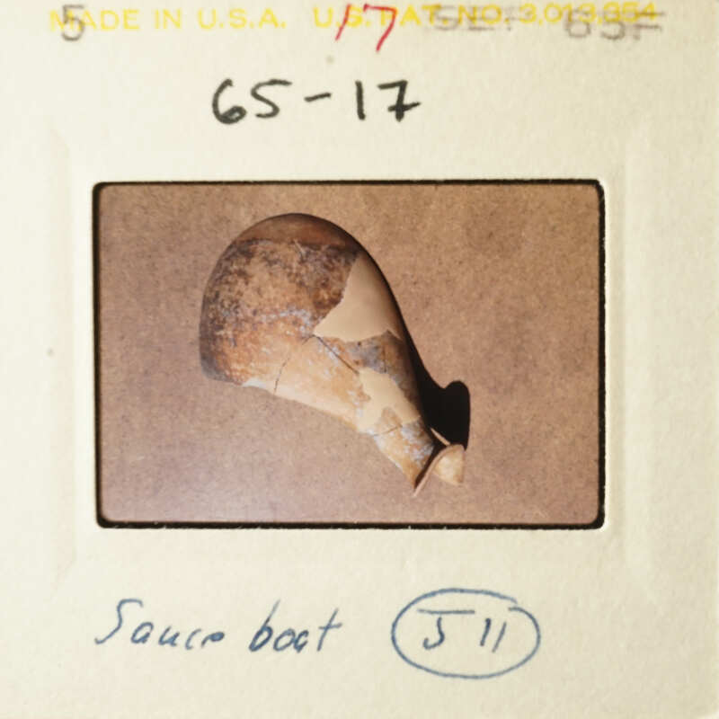 The image shows a broken pottery piece with visible cracks and missing parts, placed on a surface with a focus on its damage.