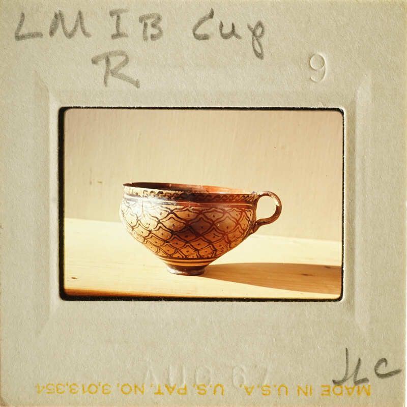 A small, intricately designed ceramic cup with a handle on a light surface.