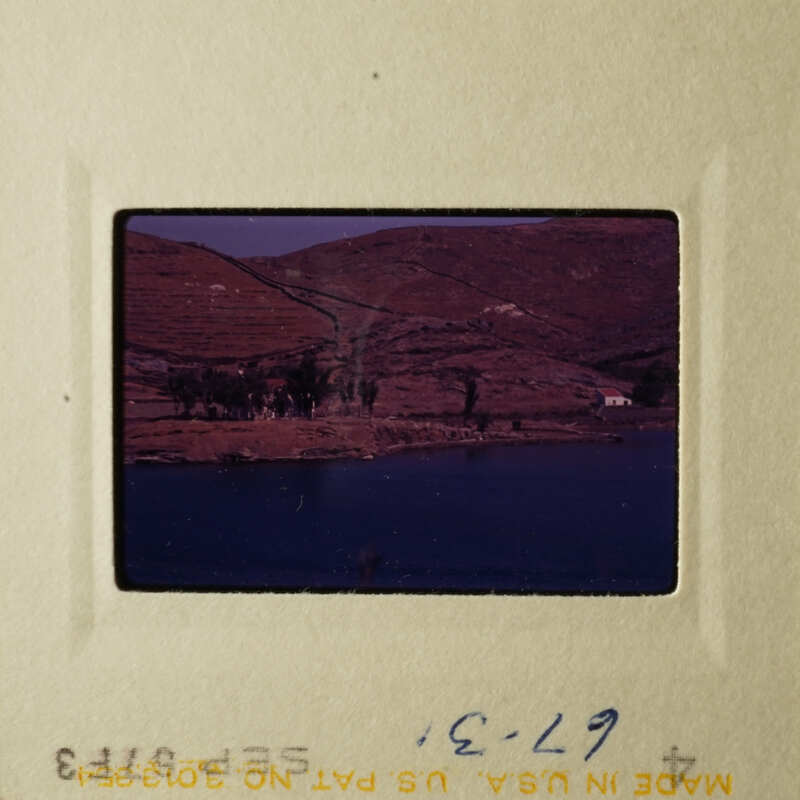 A scenic view of a body of water with a village and hills in the background, taken from an elevated perspective.