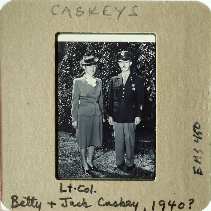 A man and woman, possibly a couple, dressed formally with military insignia on his uniform, standing together outdoors.