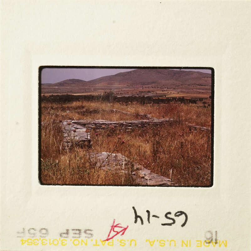 Old stone ruins in a dry landscape with mountains in the background.