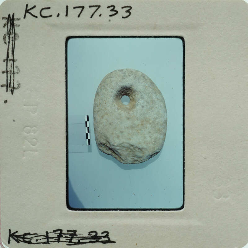 A small, round stone with a hole through it, photographed and placed on a white surface.