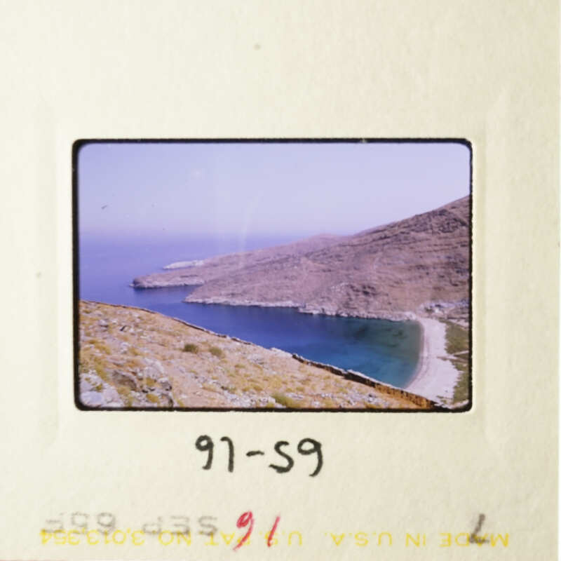 A photograph of an old slide featuring a scenic view of a coastal landscape with a clear sky, a large body of water, and a rocky shoreline.