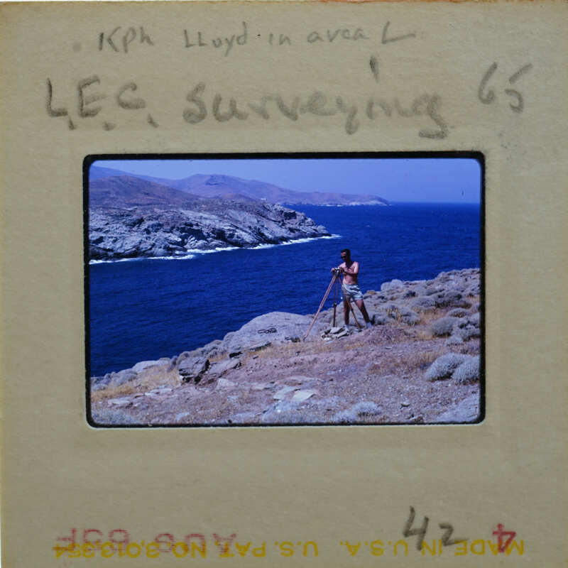 A man standing on a cliff overlooking the ocean, with mountains in the background.