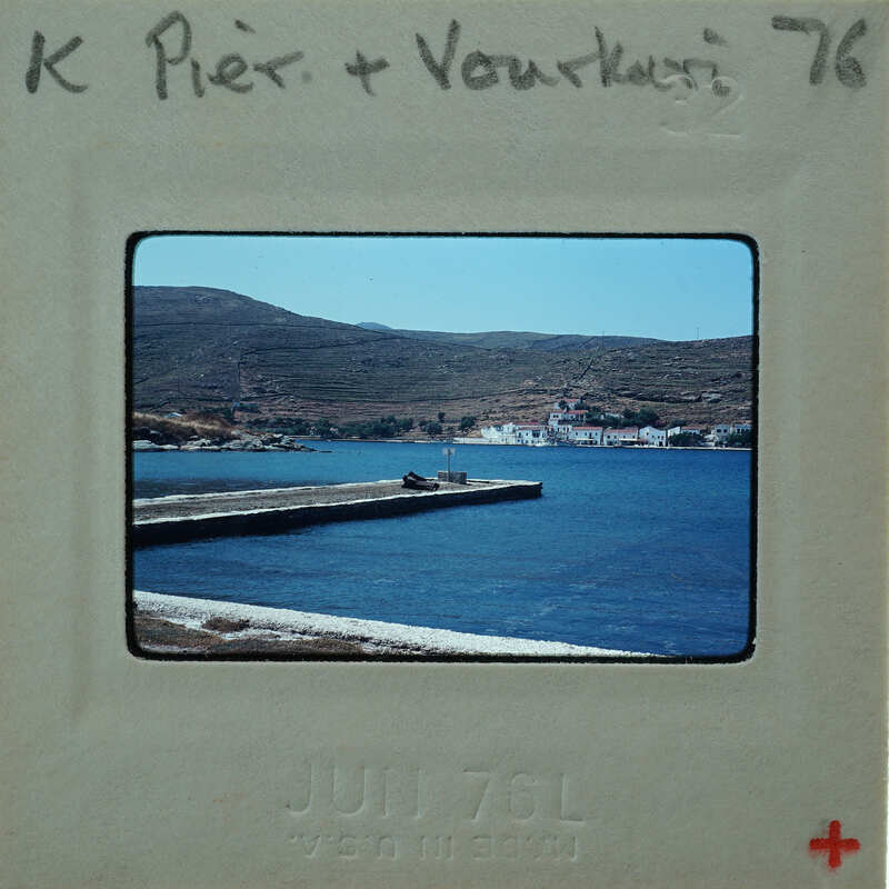 A vintage photo of a harbor with boats and hills in the background, encased in a film strip holder.