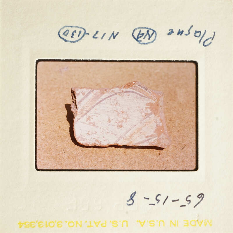 A photograph of an ancient pottery shard with visible writing on it, displayed against a light background.