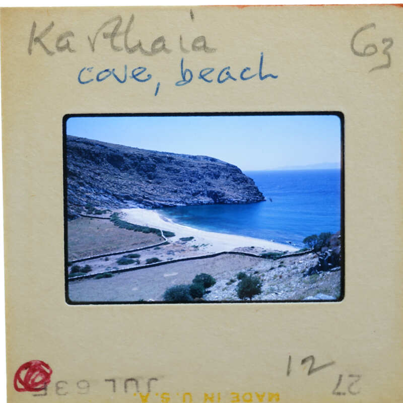 A slide of a serene beach with clear blue water, rocky cliffs, and lush greenery.