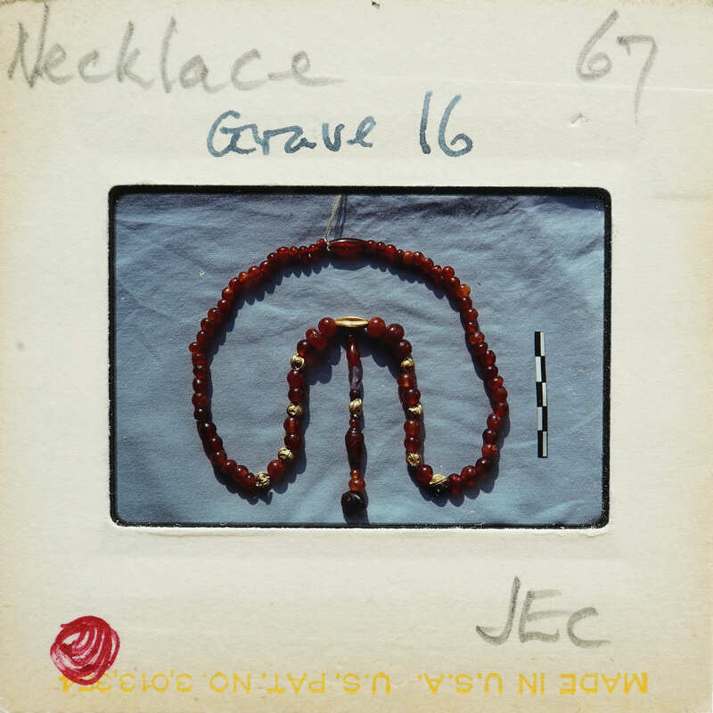 Red bead necklace with a gold pendant on a blue background, photographed on an old film negative.