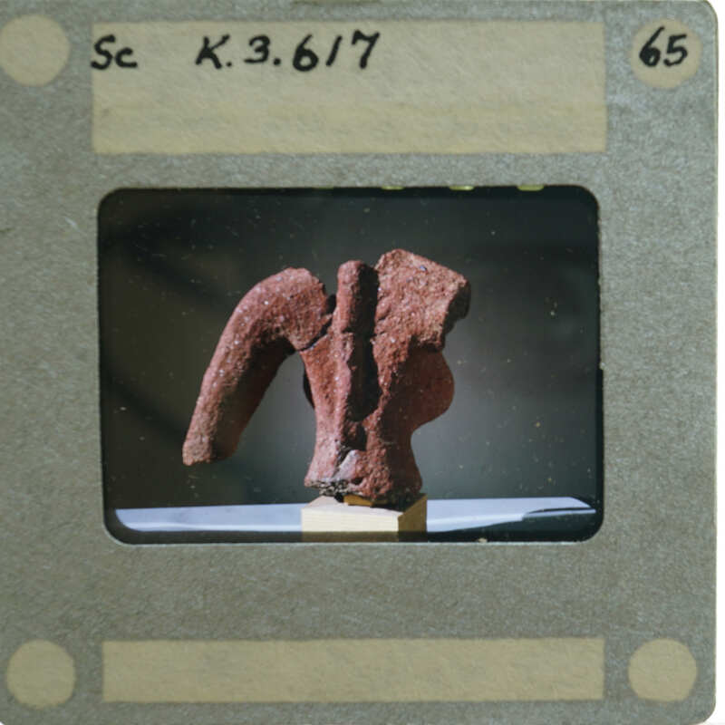 A photograph of a clay figurine torso, displayed on a stand.