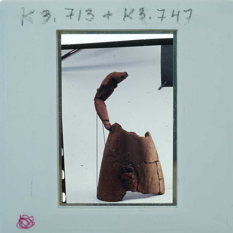 This is a photograph of an abstract sculpture with a curved form and rough texture, displayed against a white background.