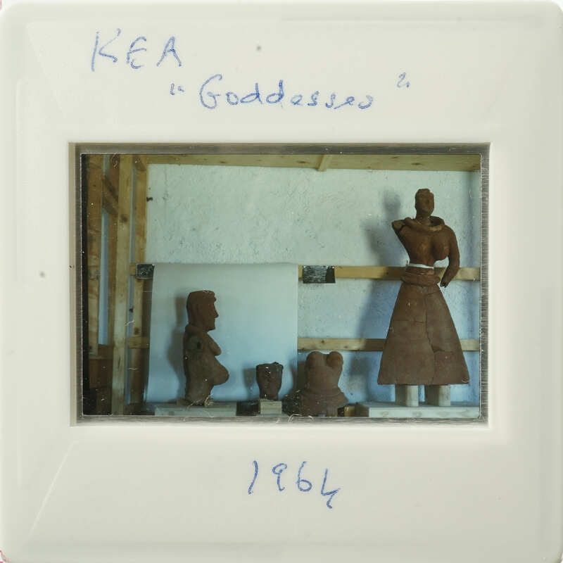 A clay figurine of a woman with a skirt, displayed on a wooden stand.