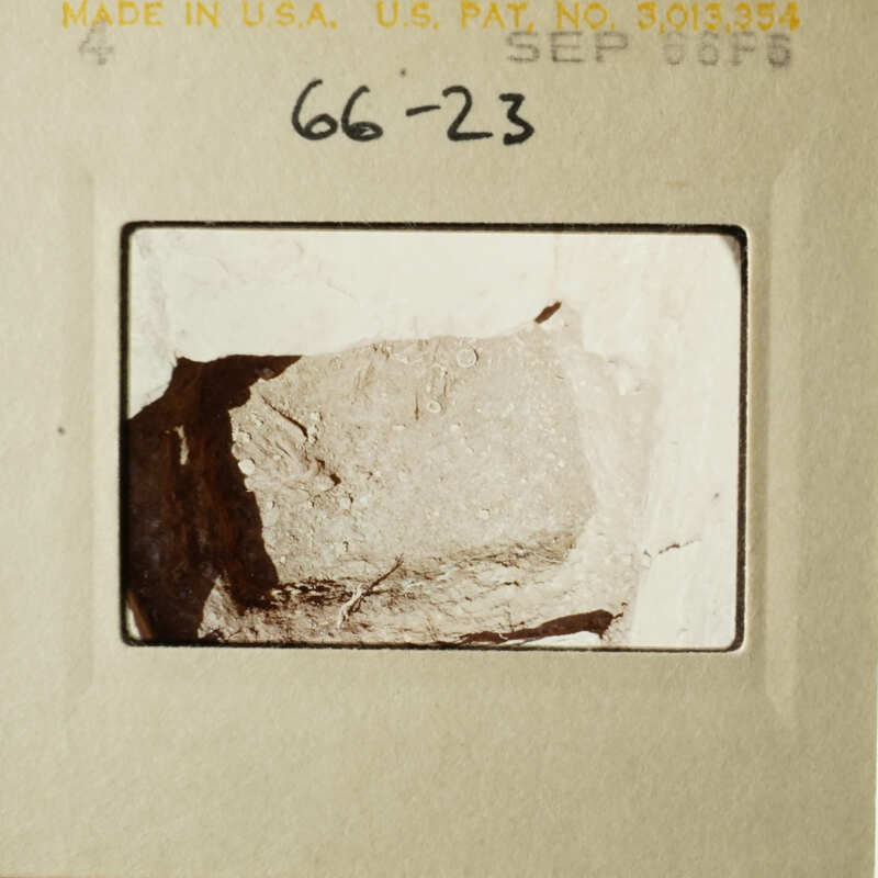 A close-up photograph of a rock sample with a yellow label and handwritten notes.