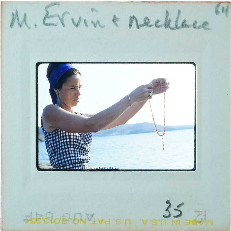 A woman holding a necklace while sitting on the water's edge.