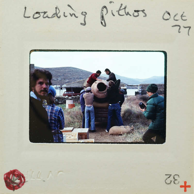 Group of people standing around a large clay pot outdoors, with mountains in the background.