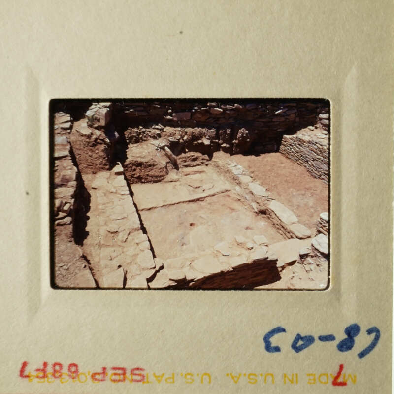 The photo shows an ancient stone structure, possibly a temple or shrine, with remnants of walls and columns, set within a natural landscape.