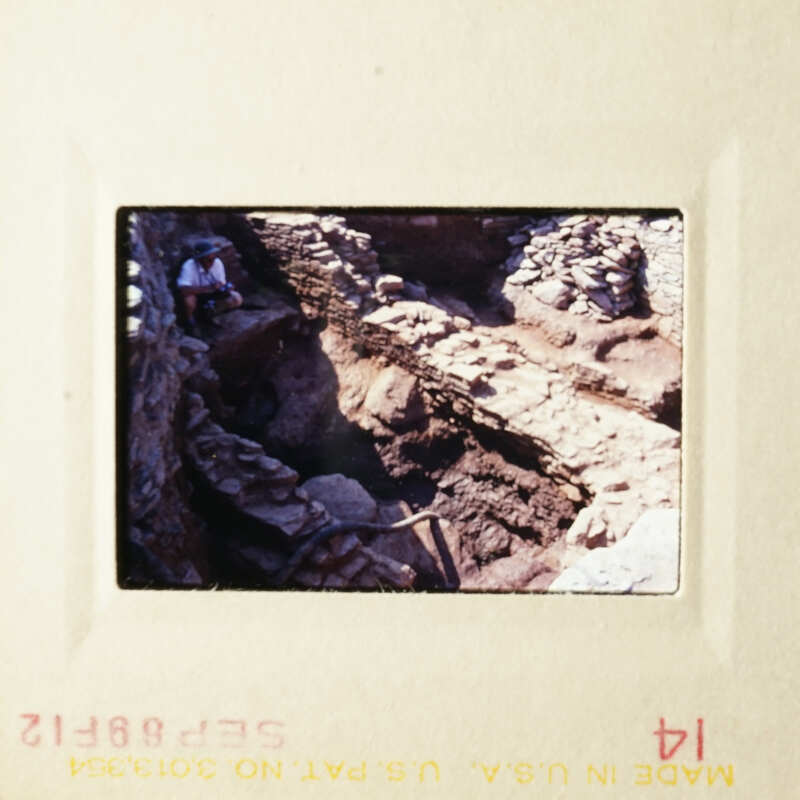 An archaeological site with stone ruins, featuring an excavation area and a person standing nearby.