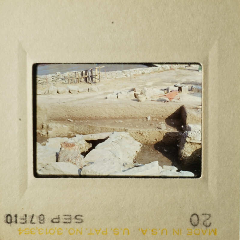 The photo shows a rocky beach scene with construction materials and equipment, possibly indicating ongoing work on the shoreline.