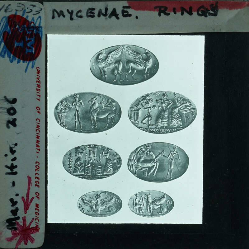 A collection of ancient rings with various designs and symbols on them, displayed behind a glass case.