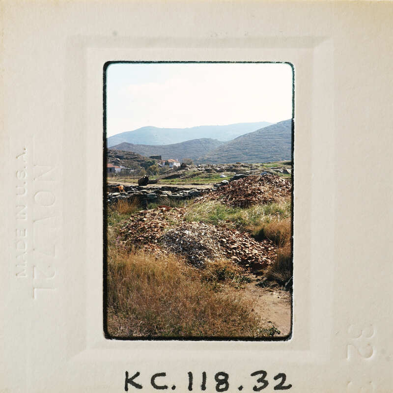 Photo of a mountainous landscape with a dirt road and scattered vegetation, presented as an old-fashioned film negative.