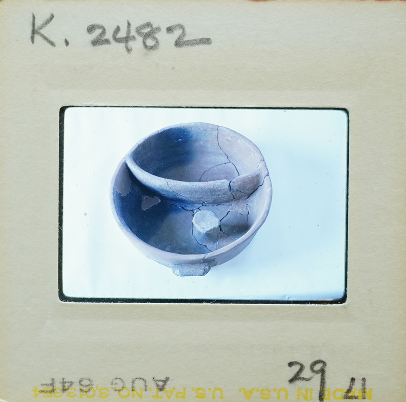 A photograph of a cracked clay pot on display with a museum label.